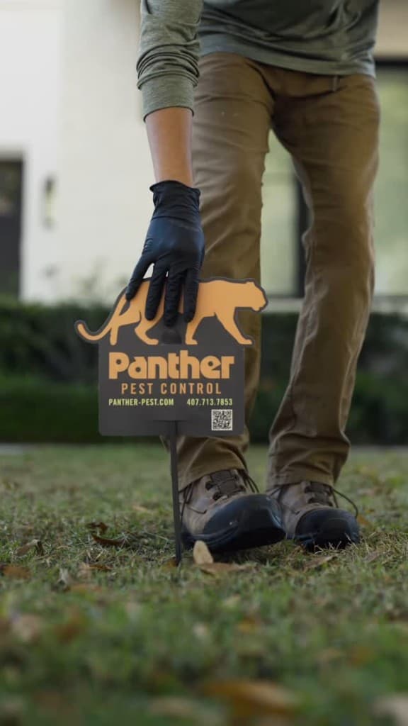 Panther Pest Control technician placing a branded yard sign in a Central Florida lawn after service