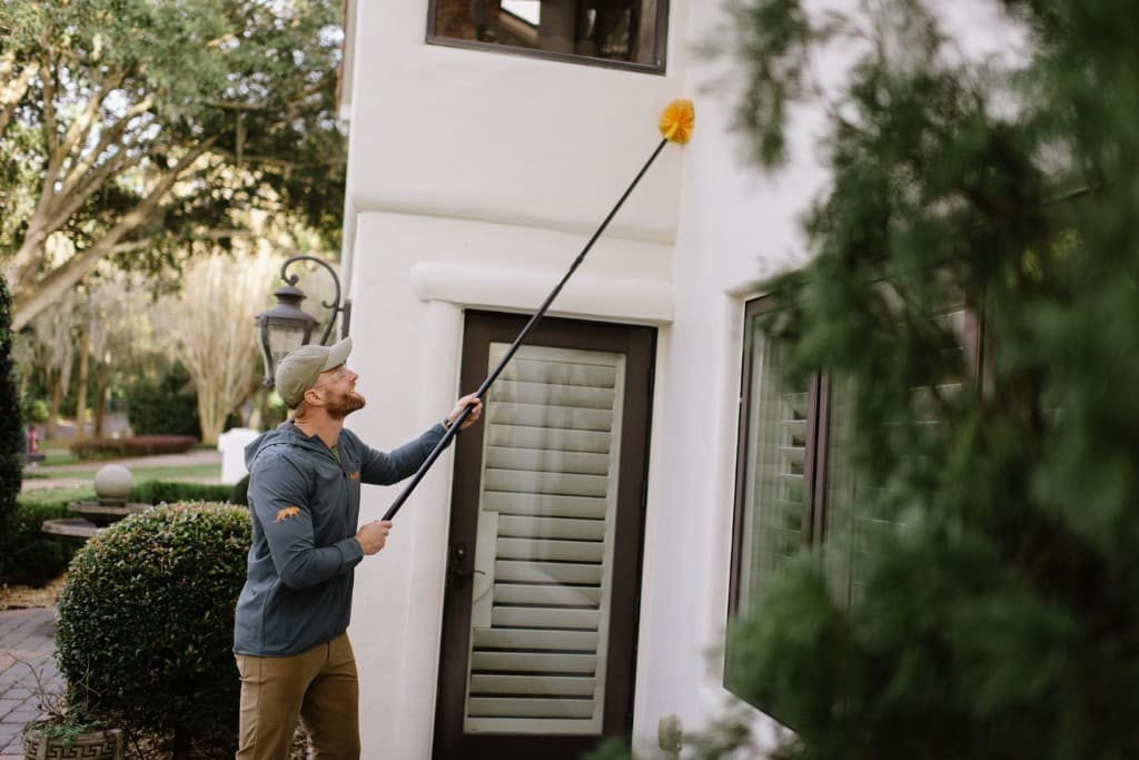 Technician removing spider webs from a home's exterior